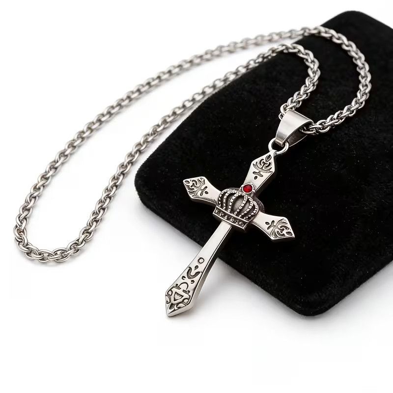 Stainless steel crown cross pendant necklace resting on black velvet pouch